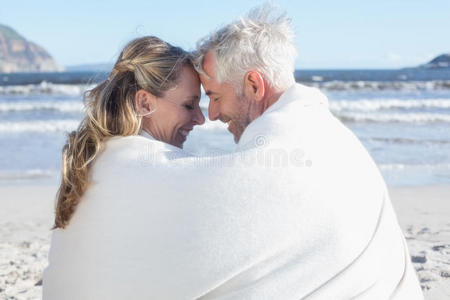 一对夫妇坐在毯子下的海滩上互相微笑