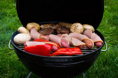 在绿色草坪上用热煤烧烤的多汁牛排汉堡香肠和蔬菜