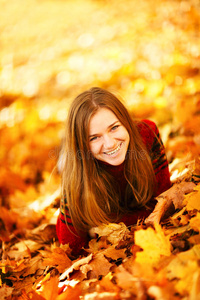 躺在秋叶中的年轻女子微笑着。
