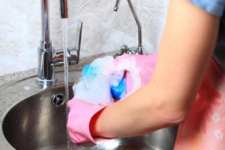 年轻的白人妇女戴着防护手套在洗碗。