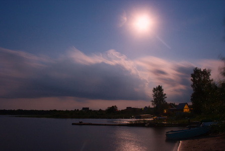 一个夏天的夜晚，塞利格湖俄罗斯的景观夜景。 天空与月亮森林在对岸的建筑物和船只一个村庄和水面与反射是可见的。 可用作