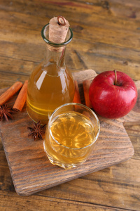 苹果酒在玻璃瓶用肉桂棒和新鲜苹果在砧板上木制的背景上