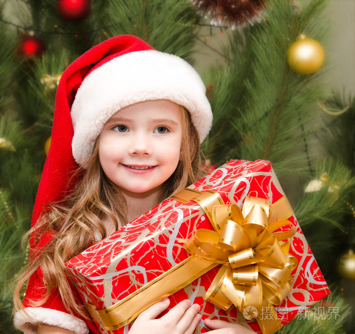 可爱微笑的小女孩在圣诞老人的帽子与礼品盒