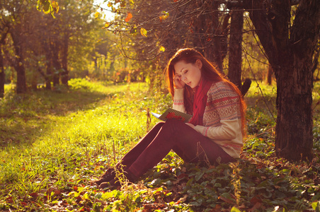 长长的红头发在树下读书的年轻女子