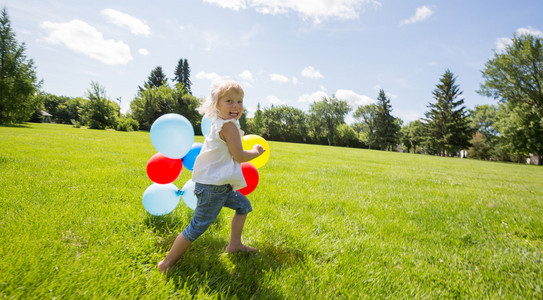 五颜六色的气球在草地上运行的女孩