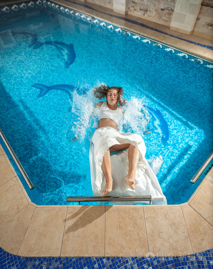 穿好衣服的女人在游泳池里的地板上滑了下来摔在水中