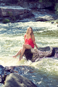 年轻女子坐在岩石在快速山区河流和溅水在夏天或早期秋季户外副本空间背景