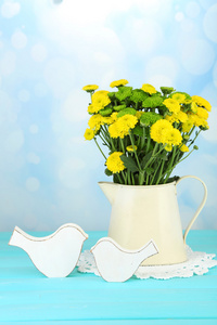 黄色和绿色的花，插在花瓶里的木桌前，在明亮的背景上