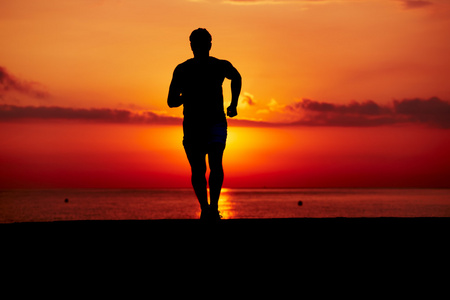 在橘红色的日出，男运动员与肌肉发达的身体，在早上慢跑 有吸引力慢跑者在行动 健身和健康的生活方式的概念对海滩上慢跑运动转轮的