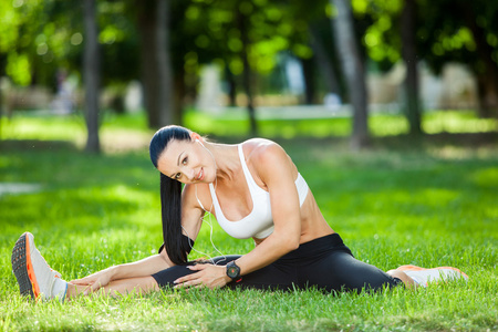美丽的运动女人做拉伸运动健身在城市公园在绿色的草地。瑜伽姿势