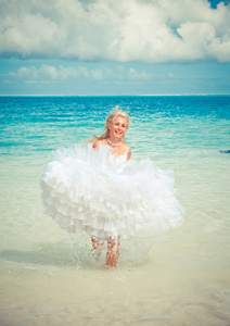 在新娘的礼服的年轻漂亮的女人在海浪上运行