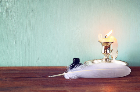 低关键图像的白色羽毛，墨水瓶和旧木桌上的蜡烛
