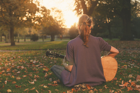 妇女坐在草地上演奏吉他在日落