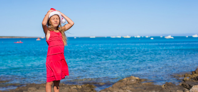 可爱的小女孩，在圣诞老人的帽子，在度假海滩上