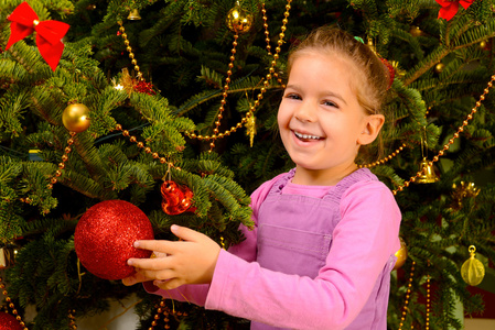可爱的蹒跚学步的女孩举行装饰圣诞玩具球