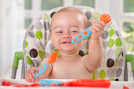 快乐微笑的可爱的宝宝举行勺子和叉子