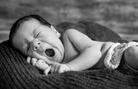 可爱的新生儿打呵欠躺在毯子上