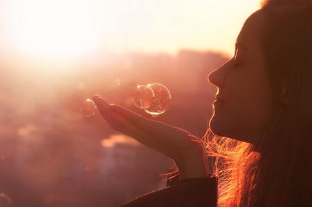 年轻女子许愿.在日落时城市景观背景照片