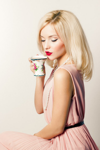 美丽微笑快乐优雅的女孩穿着粉红色的连衣裙在复古风格的红色唇膏饮料茶咖啡的小杯子