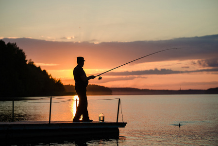 在日落时从桥上走过的湖面上钓鱼的人