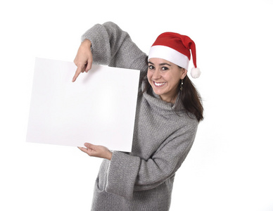 年轻甜美拉丁女人在圣诞老人帽子指向空白广告牌
