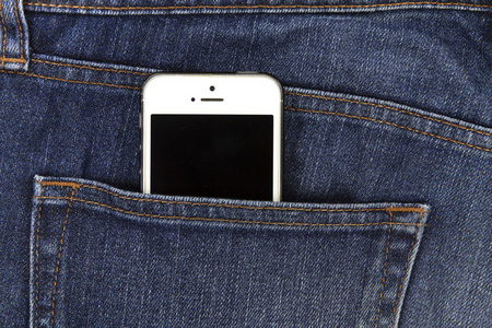 移动白色手机在口袋中的蓝色牛仔布的一部分