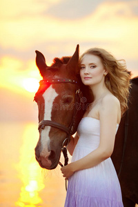 日落时在海滩上骑马的美女。在海边阳光下牵着一匹马的小女孩。