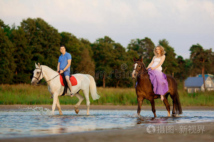 两个骑马的人在海滩上日落时骑马情侣骑马一个年轻的男人和一个漂亮的