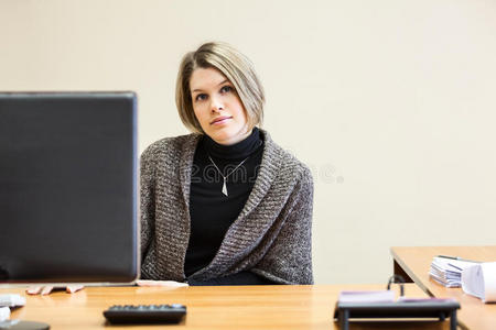 冷静的年轻女人坐在电脑屏幕后面的桌子上
