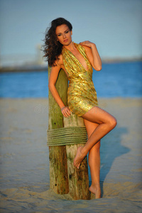 海滩上穿着金色奢华礼服的时装模特。