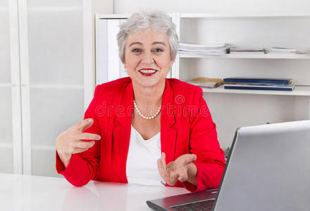 坐在办公桌旁，面带微笑的迷人的年长女商人