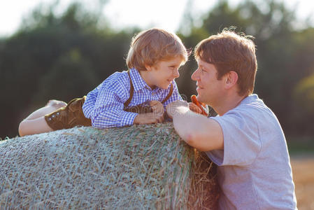 年轻的父亲和他的小儿子在黄色的干草地上玩耍