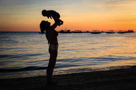 快乐的妈妈和宝宝在日落海滩玩得开心