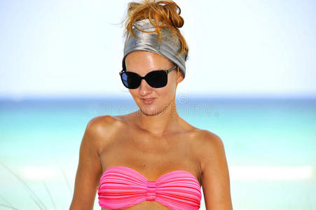快乐的年轻漂亮的女人穿着粉色比基尼在天堂海滩摆姿势