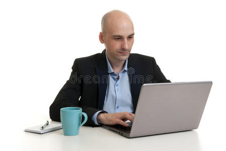 商人坐在办公桌旁，工作在笔记本电脑上