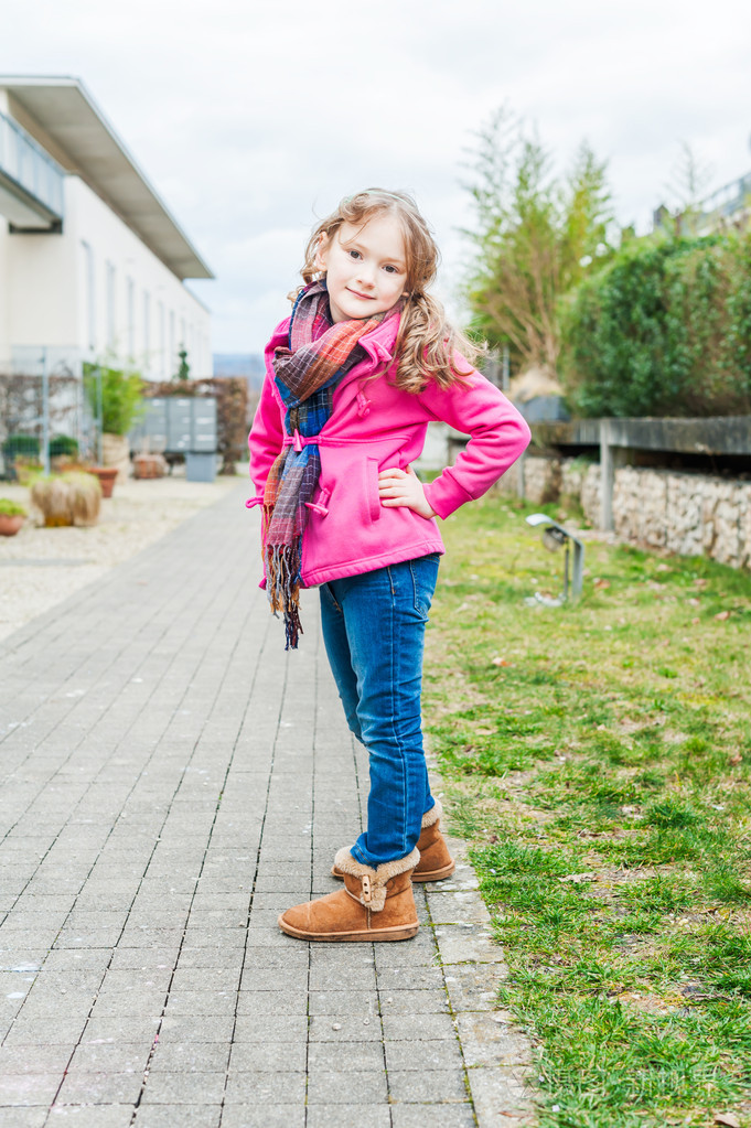 一个可爱的小女孩,穿着牛仔裤,靴子和粉红色的外套的室外肖像