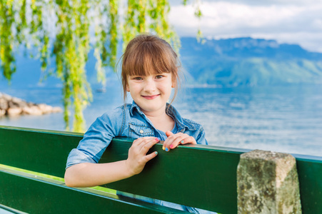 可爱的小女孩，美丽的景色的湖泊和山脉上有一张长椅上的室外肖像