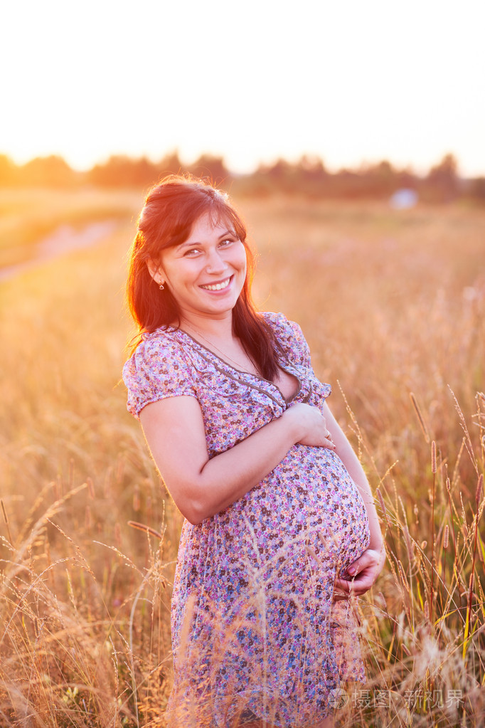 美丽快乐年轻孕妇女孩在字段中微笑和