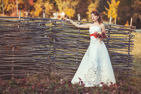 新娘站着柳条栅栏附近的花束