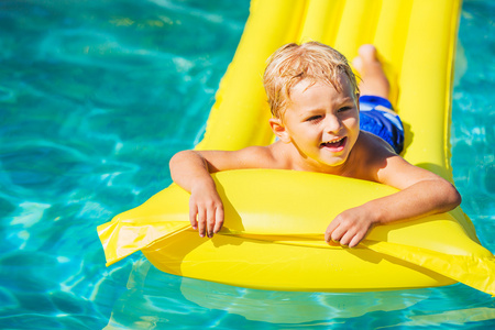 男孩在黄色的筏子上的游泳池里放松和娱乐