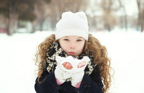 小女孩微笑着，在一个公园在寒冷的天气中吹雪