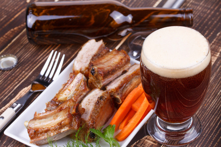 玻璃和瓶啤酒。烤的排骨和木制背景上的新鲜胡萝卜