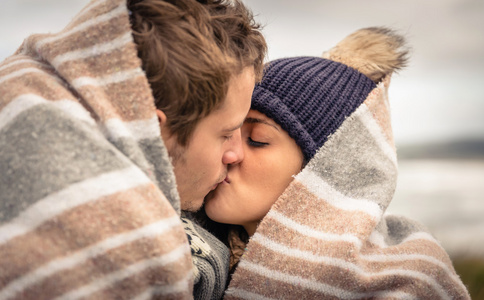 年轻的夫妇在毯子下户外接吻，在一个寒冷的日子