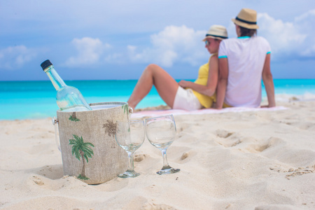 瓶白葡萄酒和两杯背景幸福的夫妇，在沙滩上