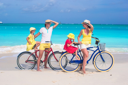 在热带沙滩上的四个骑自行车的年轻家庭