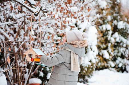 可爱儿童女孩把种子在白雪皑皑的冬季花园喂鸟器
