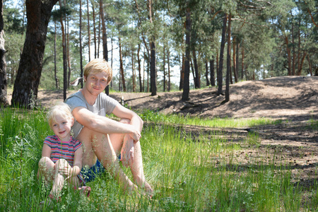 女儿和她的父亲在夏天在树林里坐在草地上