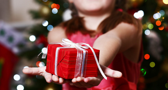 小女孩拿着礼物盒在圣诞树旁，光棍