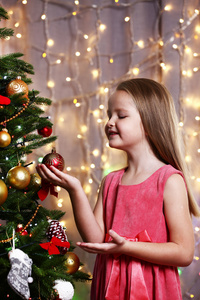 小女孩在明亮的背景下装饰圣诞树