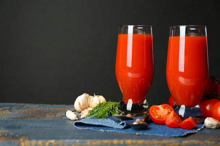 美味的番茄汁和新鲜的西红柿在桌子上，在灰色的背景上的眼镜